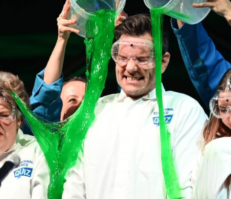 Man getting green slime poured on him while wearing National science Quiz branded PPE